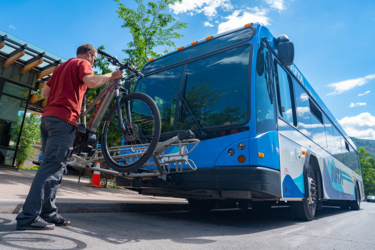 A man in a red shirt straps his bike to the front of a RFTA bus on a sunny day