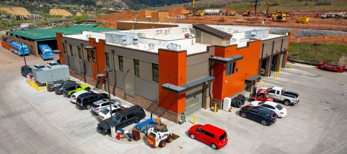 A modern building with grey and orange walls surrounded by cars and construction equipment